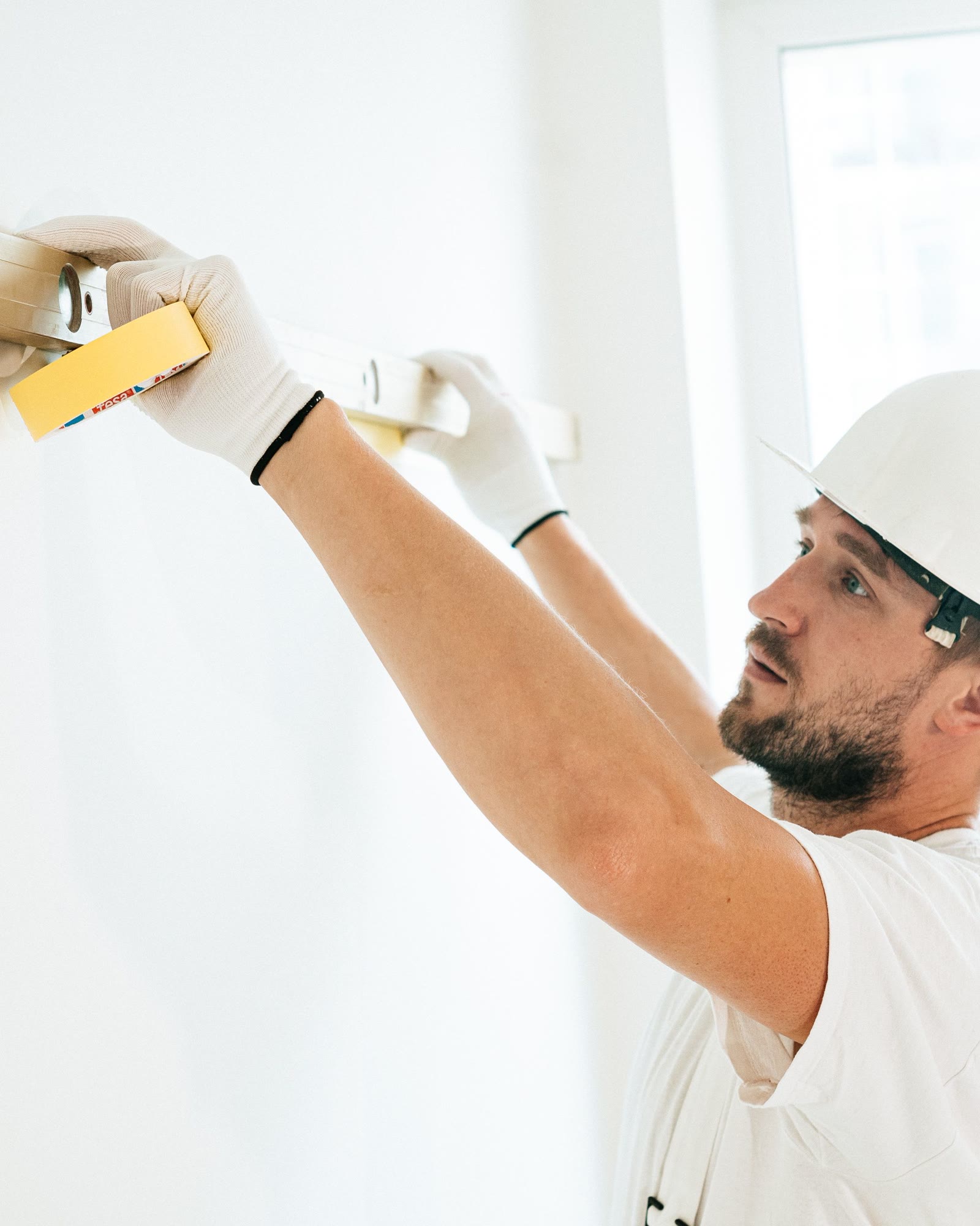 A gloved hand holding a spirit level against a newly finished wall.
