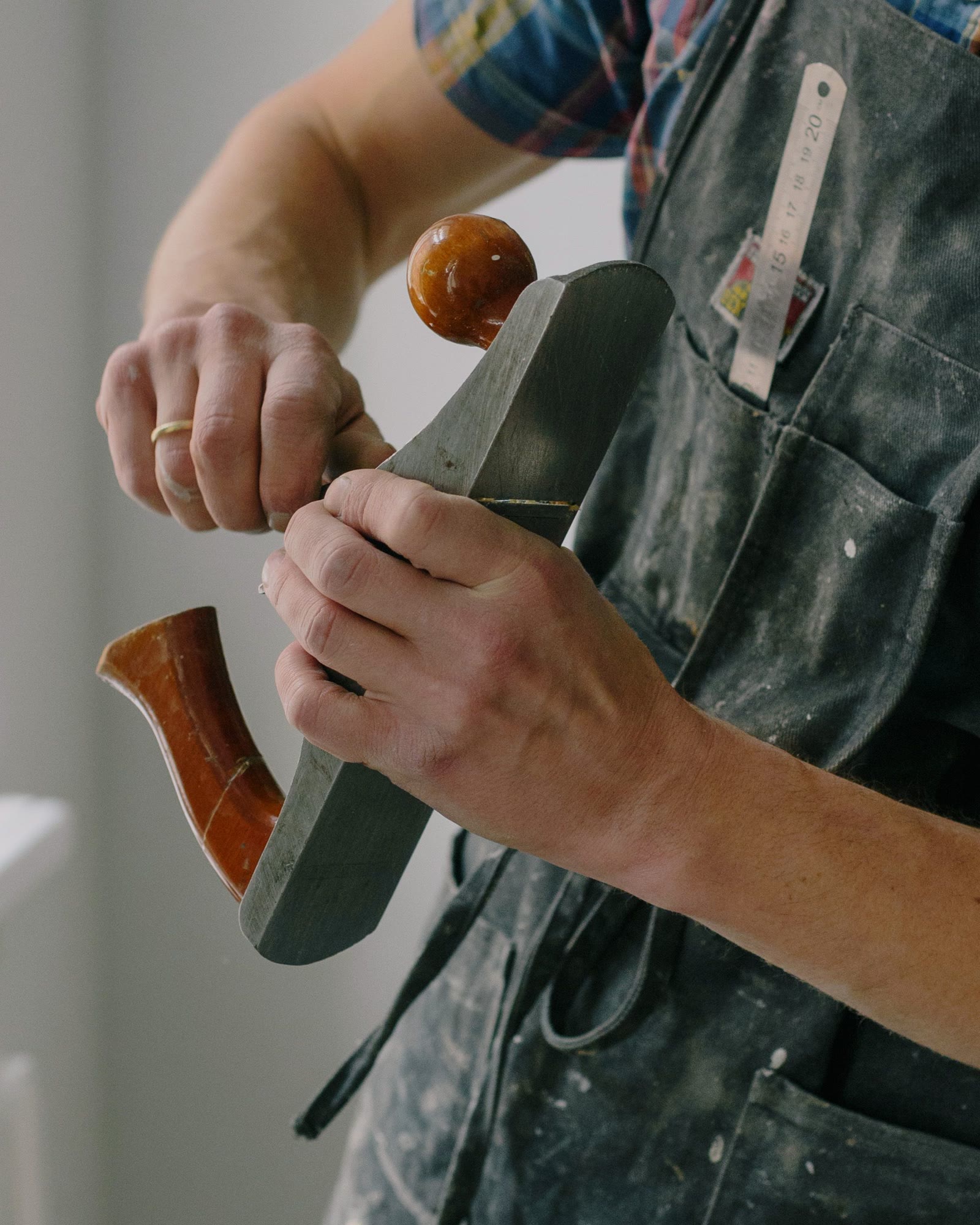 Hands guiding a wooden smoothing plane, a folding rule in the pocket of a canvas apron.