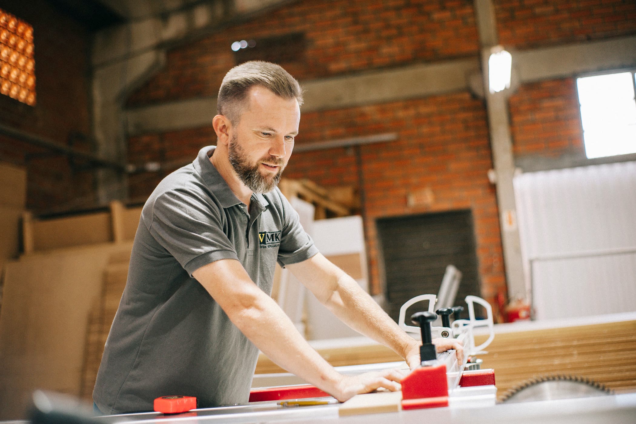 A builder feeding a length of timber through a saw bench in a brick workshop.